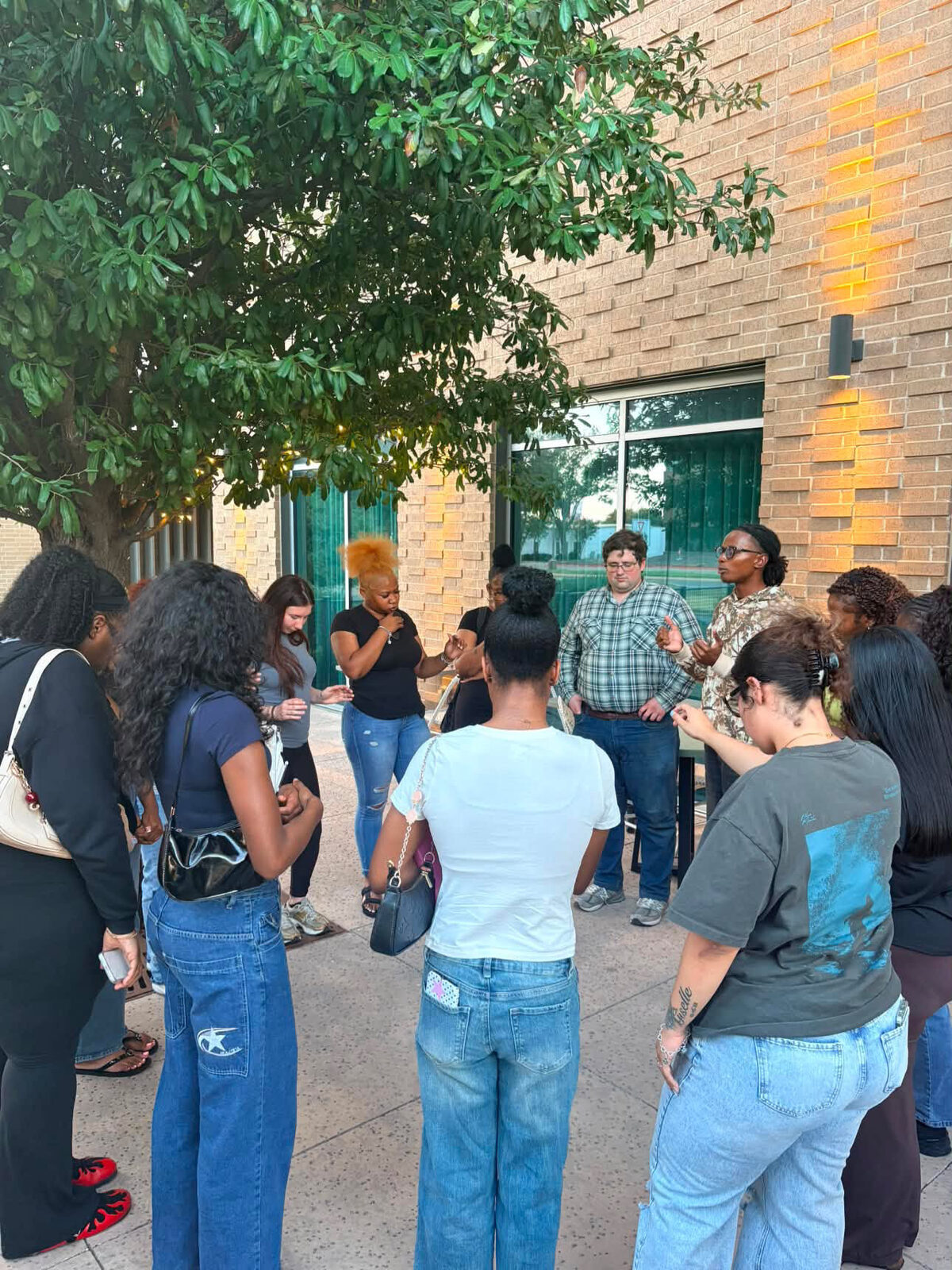 Club Polis members standing in a circle in prayer outside a building in the DFW Metroplex